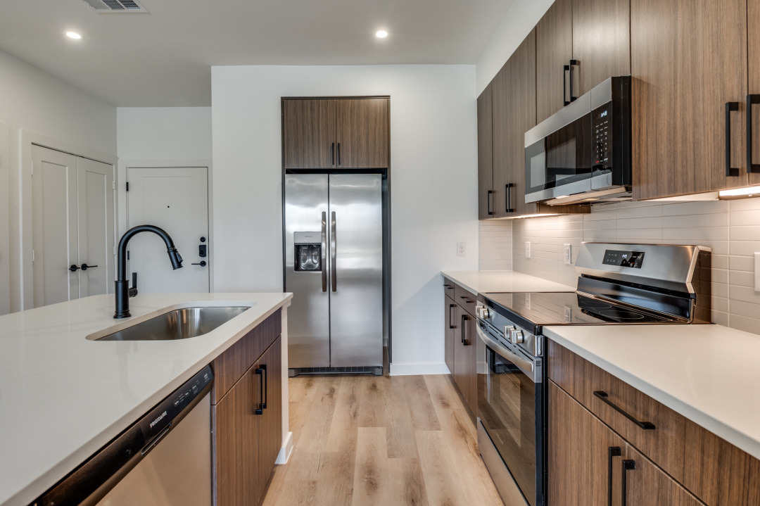 Kitchen interior showing quartz countertops, stainless steel appliances, undermount sink, and wood-style flooring